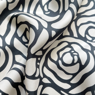Close-up of luxurious silk scarf fabric with charcoal grey abstract rose pattern on white background, showing elegant texture and sheen