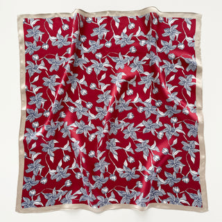 Square silk bandana scarf with vibrant red background featuring blue floral botanical pattern and cream-colored border, displayed flat.