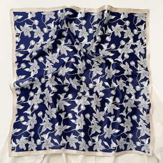 Square silk bandana scarf with deep navy blue background featuring elegant white floral pattern and light beige border trim