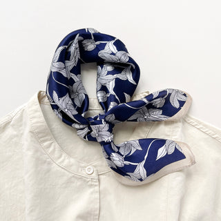 Navy blue silk bandana scarf with white floral leaf pattern tied elegantly around the collar of a cream blouse, showcasing versatile styling