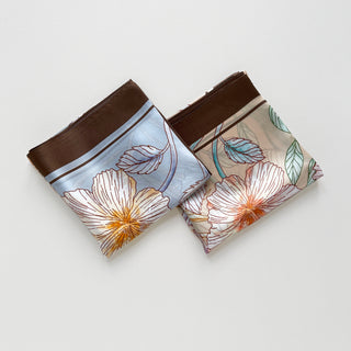 Two folded silk bandana scarves with floral designs - light blue and beige versions with delicate flower patterns and rich brown borders