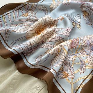 Light blue silk scarf with elegant floral design and butterfly pattern, featuring rich brown border trim and delicate gold accents