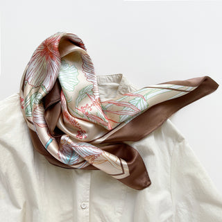Beige silk bandana scarf with delicate red floral outlines, green leaf details, and rich brown border, elegantly draped on white shirt.