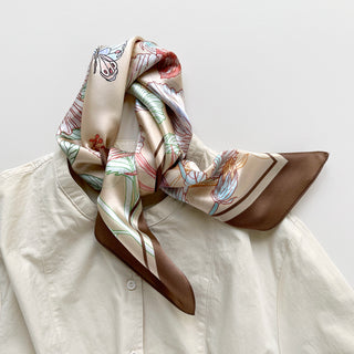 Beige silk bandana scarf with delicate floral print in light blue and red tones, featuring brown border, elegantly draped on white shirt collar