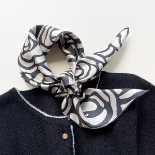 Silk bandana scarf with charcoal grey abstract rose pattern on white background, elegantly knotted on a dark coat collar