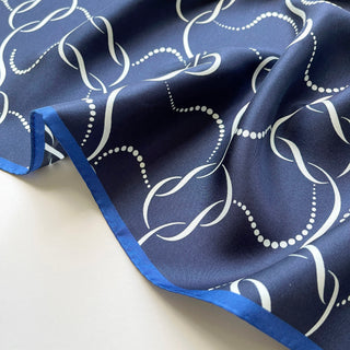 Navy blue silk scarf with elegant white chain-link pattern featuring royal blue hand-rolled edges and silky smooth texture