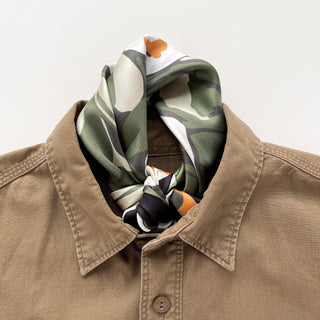 Green and charcoal black Berry Blossom silk neckerchief with cream and orange details, knotted inside a tan shirt collar.