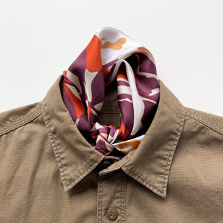 Berry-purple, orange and cream Berry Blossom silk neckerchief knotted inside a tan shirt collar.