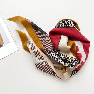 Diamond-shaped cashmere silk scarf featuring vibrant red, mustard, and beige colors with leopard print pattern and striped accents, elegantly draped.