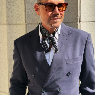 Man wearing a navy paisley patterned silk square neckerchief by LuluLane with a navy suit and sunglasses showcasing a refined sharp look.