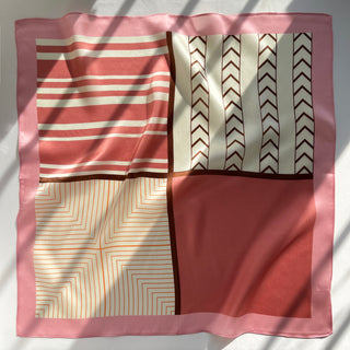 Pink silk bandana with geometric design featuring four quadrants of patterns: coral stripes, chevron arrows, concentric squares, and solid pink, all with shiny finish.