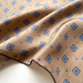 Taupe silk neckerchief with blue diamond medallion pattern, featuring hand-rolled edges and luxurious twill texture, showcasing the fabric's elegant drape