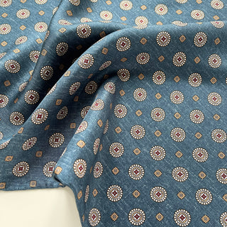 Denim blue silk neckerchief with elegant medallion pattern featuring cream circles, burgundy centers, and gold accents, draped to show luxurious texture