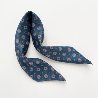 Denim blue silk neckerchief with taupe medallion pattern, elegantly folded to display its 53cm hand-rolled edges and classic design