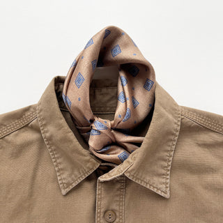 Taupe silk neckerchief with blue diamond medallion pattern styled with a knot at the collar of a khaki button-up shirt