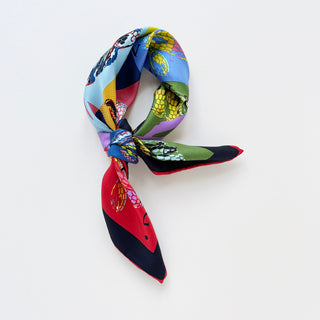 Colorful silk bandana scarf with vibrant snake print in blue, red, green, and yellow geometric blocks, tied in classic bandana style