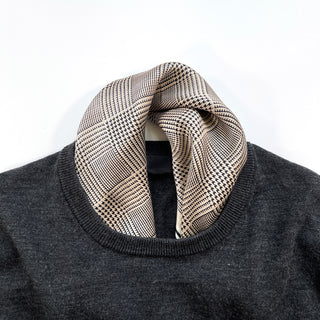 Black houndstooth silk scarf with beige background elegantly draped around a dark sweater neckline, displaying its luxury pattern and texture