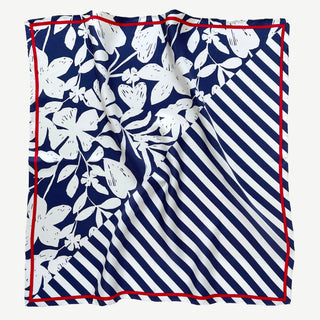 Square silk scarf with navy blue and white design featuring floral patterns and diagonal stripes, bordered with a bright red trim