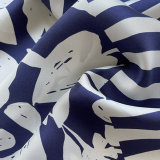 Close-up of luxurious navy blue and white silk scarf with floral pattern and geometric stripes, showing the fine texture and sheen of 100% pure silk fabric