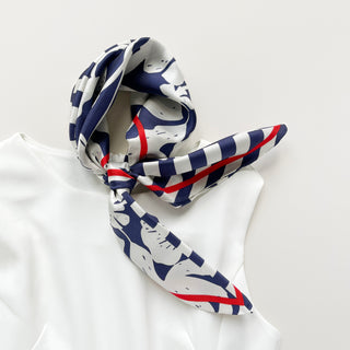 Elegantly tied silk scarf with navy blue and white floral pattern, striped design, and red border, displayed on white fabric surface