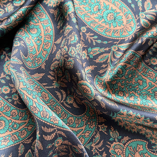 Luxurious silk scarf with intricate paisley pattern in black, green, and gold tones, showcasing shimmering fabric with elegant floral motifs