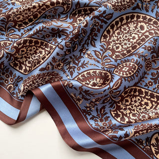 Light blue silk scarf with intricate brown paisley pattern, featuring elegant floral motifs and a contrasting brown and blue striped border
