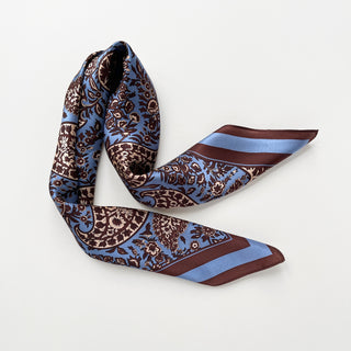 Men's silk neckerchief with blue and brown paisley pattern, elegantly draped to showcase luxurious fabric and intricate floral design.