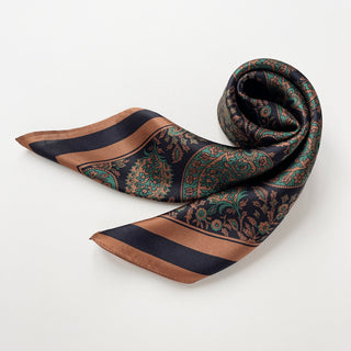 Elegant silk scarf featuring intricate paisley pattern in black, green, and copper tones with striped border, displayed in a gentle curve showing texture