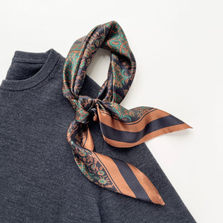 Black and green paisley silk neckerchief with copper accents draped around a dark gray sweater collar, showing intricate pattern detail
