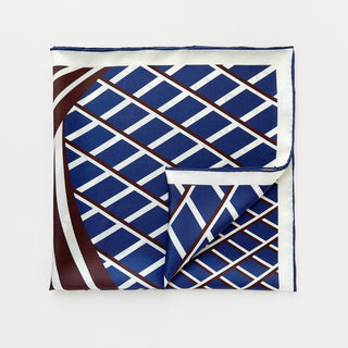 Luxurious silk pocket square featuring navy blue diamond pattern with brown diagonal lines on cream background, showing hand-rolled edges and folded corner.