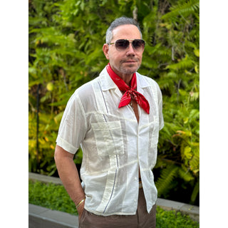 Man wearing a classic paisley pattern red bandana in a white shirt, and sunglasses with a green foliage background.