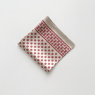 Folded silk scarf in beige with red horseshoe pattern, featuring decorative border and shiny satin finish, displayed on white background