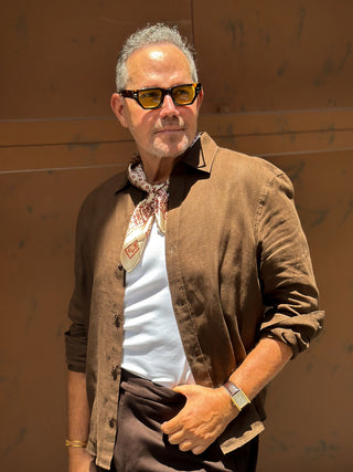 Styling example: beige men's silk scarf with red horseshoe pattern worn with white t-shirt and brown shirt and amber sunglasses in outdoor setting