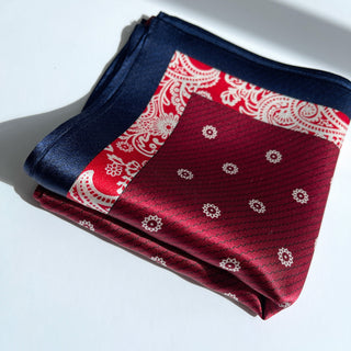 Folded silk bandana scarf with burgundy, red, and navy blue sections featuring delicate white floral and paisley patterns on a white surface.