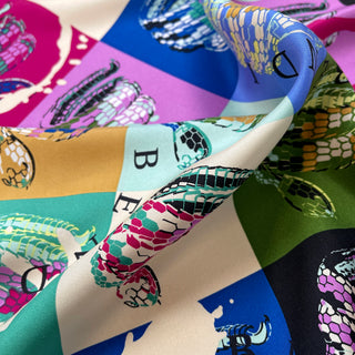 Luxurious silk scarf with colorful geometric blocks in blue, pink, green, and beige, featuring stylized snake prints in various colors with textured scales