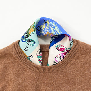 Colorful silk scarf with snake print in blue, mint, pink and yellow tones styled inside a camel sweater neckline, showing vibrant patterns