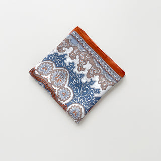 Folded silk scarf with blue and orange baroque pattern, featuring ornate paisley designs and intricate geometric motifs on white background