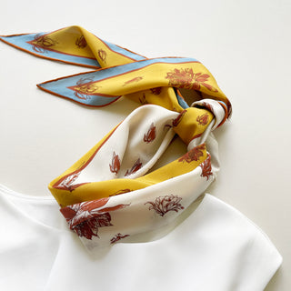 Close-up of floral diamond silk scarf tied around a white dress, showcasing its vibrant yellow and ivory floral pattern with blue and rust border.
