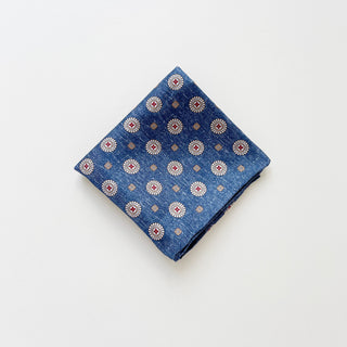 a luxury folded silk neckerchief with circular medallion pattern in denim blue with hand-rolled edges.