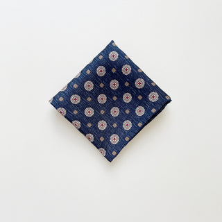 a luxury folded silk neckerchief with circular medallion pattern in dark denim blue with hand-rolled edges.