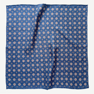 Denim blue silk neckerchief with repeating taupe medallion pattern, displayed flat showing hand-rolled edges and luxurious twill texture