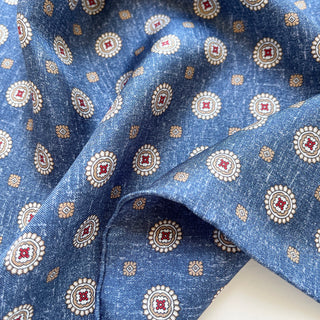 Denim blue silk neckerchief with elegant medallion pattern featuring cream circles, burgundy centers, and gold accents, draped to show luxurious texture