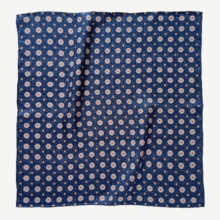 Dark denim blue silk neckerchief with repeating taupe medallion pattern, displayed flat showing hand-rolled edges and luxurious twill texture