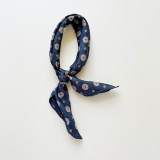 Dark denim blue silk neckerchief with taupe medallion pattern, knotted loosely on a white background