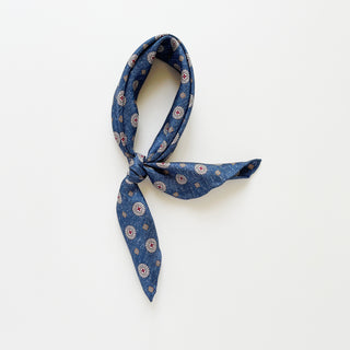 Denim blue silk neckerchief with taupe medallion pattern, knotted loosely on a white background