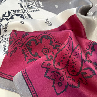 Plum red and cream silk bandana with intricate black paisley pattern, showing luxurious sheen and soft fabric texture in natural light.
