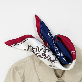 Plum red and navy blue silk bandana with white paisley pattern, elegantly draped on beige jacket collar, showcasing its luxurious sheen