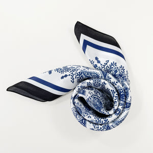 a swirling white based silk scarf with rich blue paisley pattern print featuring black edge suits for both women and men