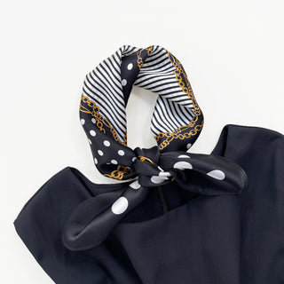 Black silk bandana scarf with white polka dots, striped pattern, and gold chain print, tied elegantly on black fabric, showcasing its 53cm square design