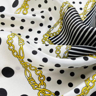 Luxury silk scarf featuring black polka dots on white with gold chain pattern and black stripes, showcasing the glossy texture and elegant design